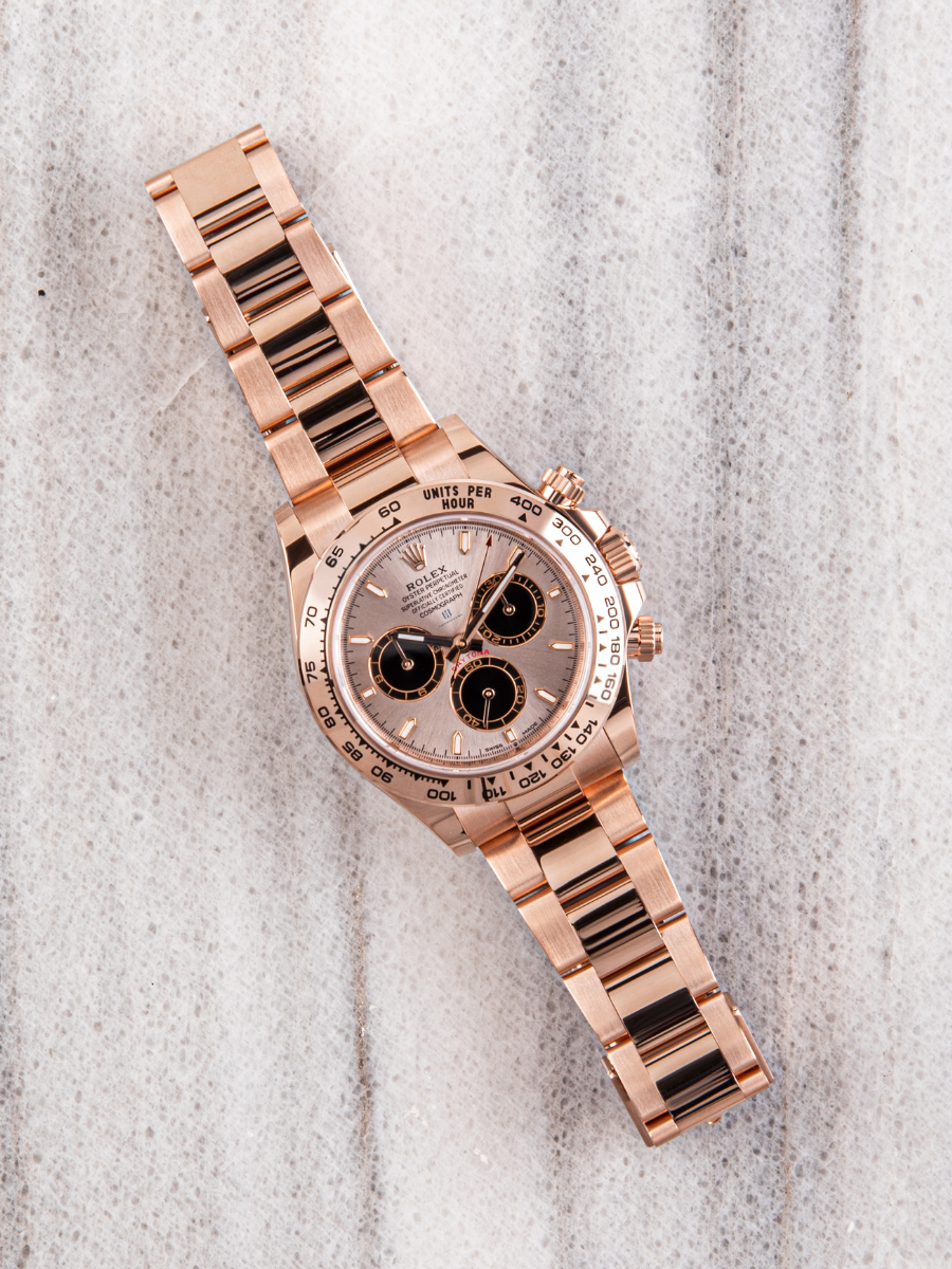 Rose gold Rolex Daytona 126505 on a textured background showcasing dial details, complications, tachymeter scale, and angled composition