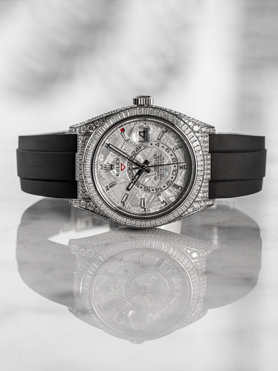 Rolex Sky-Dweller watch featuring a meteorite dial, baguette diamond bezel, and a black rubber strap, reflected on a marble surface