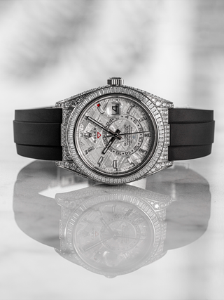 Rolex Sky-Dweller watch featuring a meteorite dial, baguette diamond bezel, and a black rubber strap, reflected on a marble surface