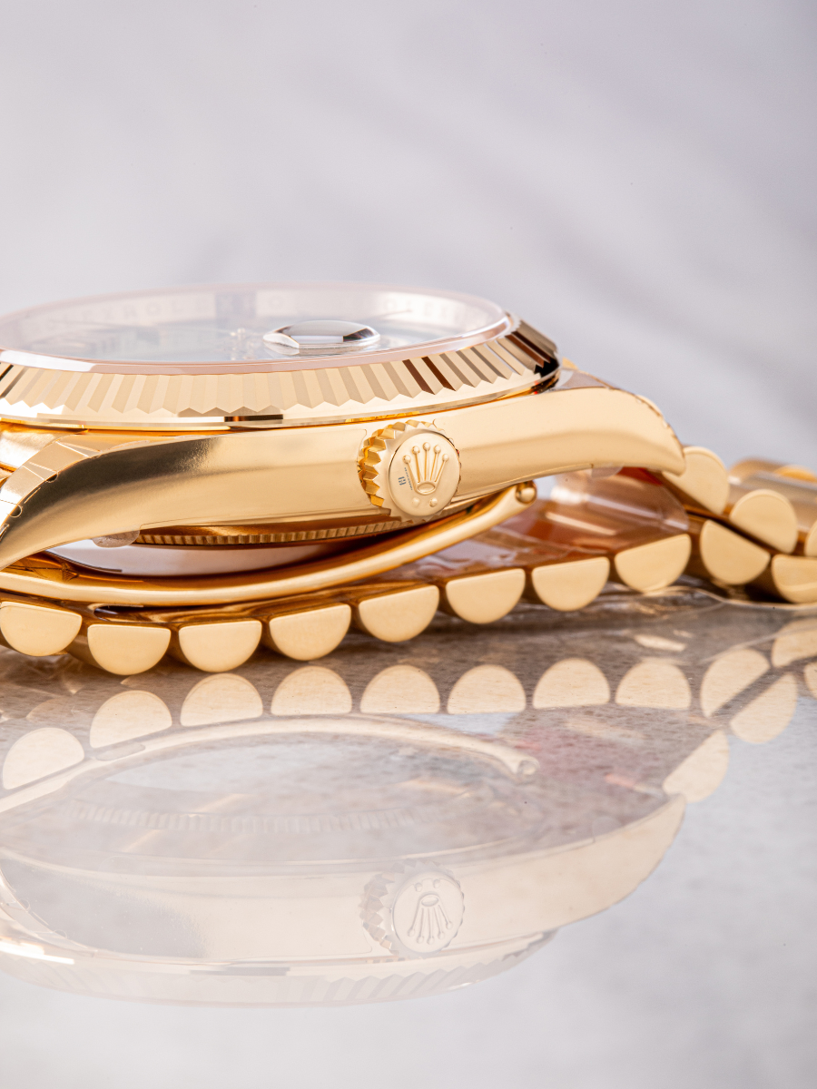 Gold crown with Rolex coronet of Rolex Day Date 228238 and the reflection of the watch on the surface